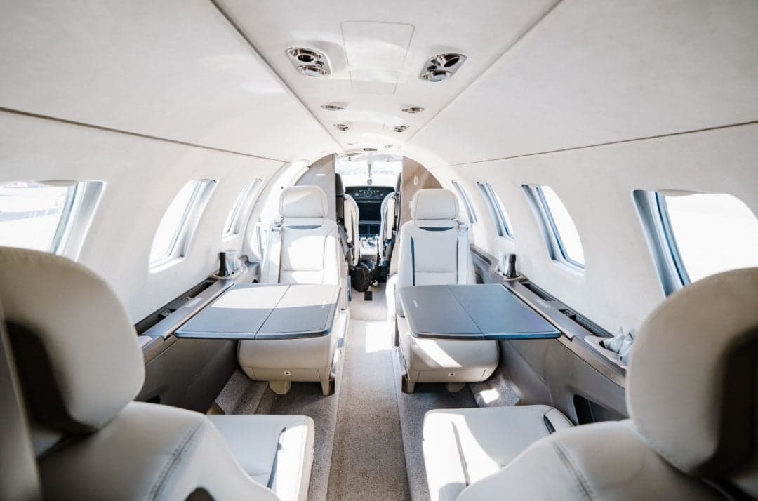 View of the interior of the aircraft cabin with white leather seats and tables.