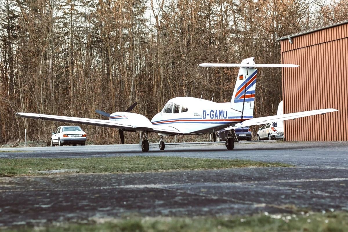 Piper Seminole D-GAMU parked on the tarmac with cars in the background.