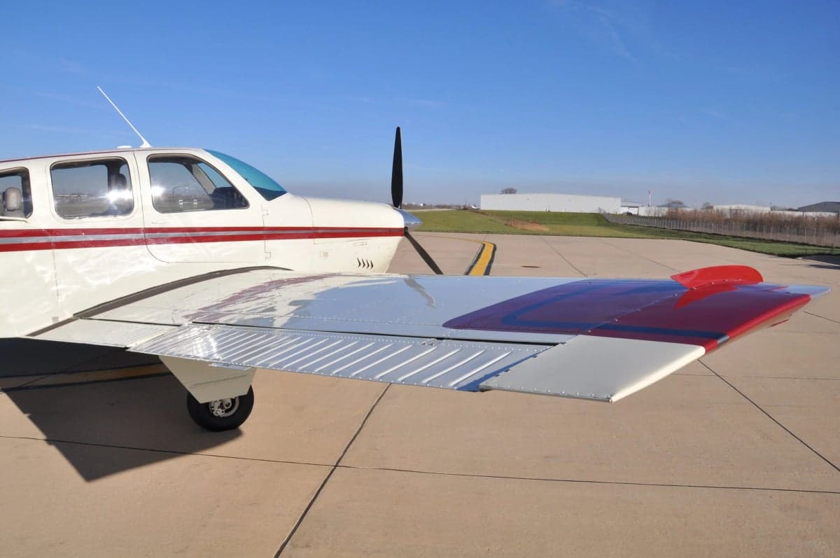 Close up of the wing and fuselage of a Beechcraft Bonanza with a red and white paint scheme.