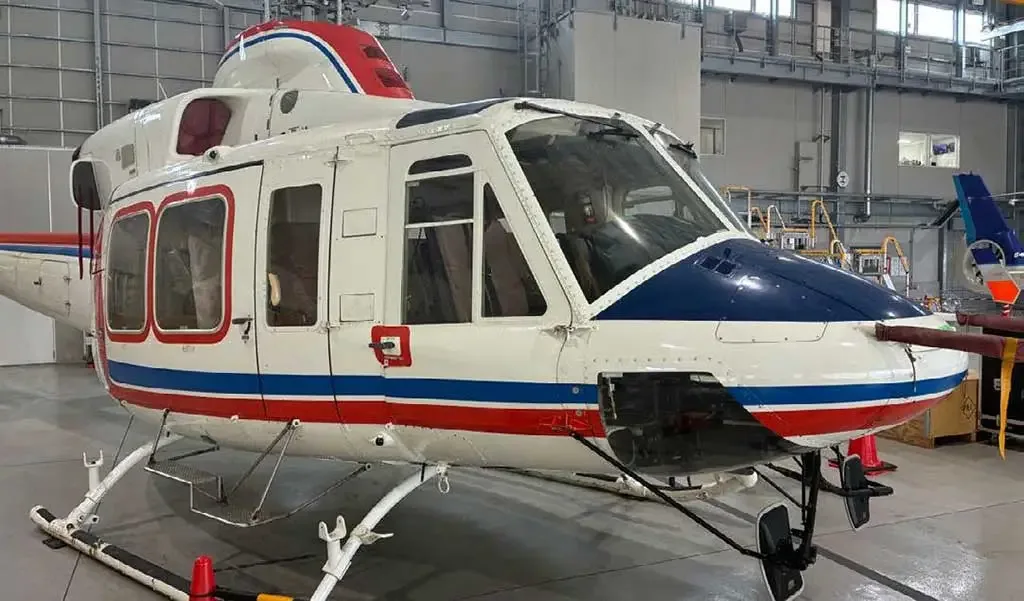 A three-quarter front view of a white helicopter with blue and red stripes, parked in a hangar.