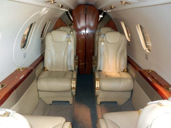 Interior view of the jet cabin with tan leather seats and wood trim.