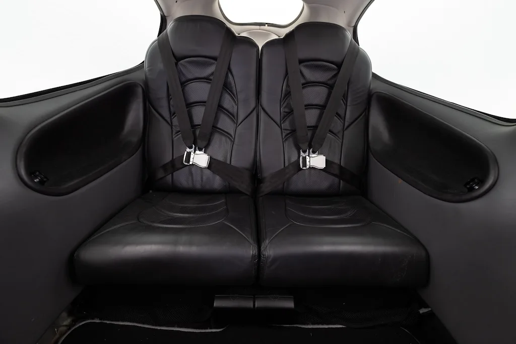 The black leather rear cabin seats of a Cirrus aircraft, showing two seats with harnesses.