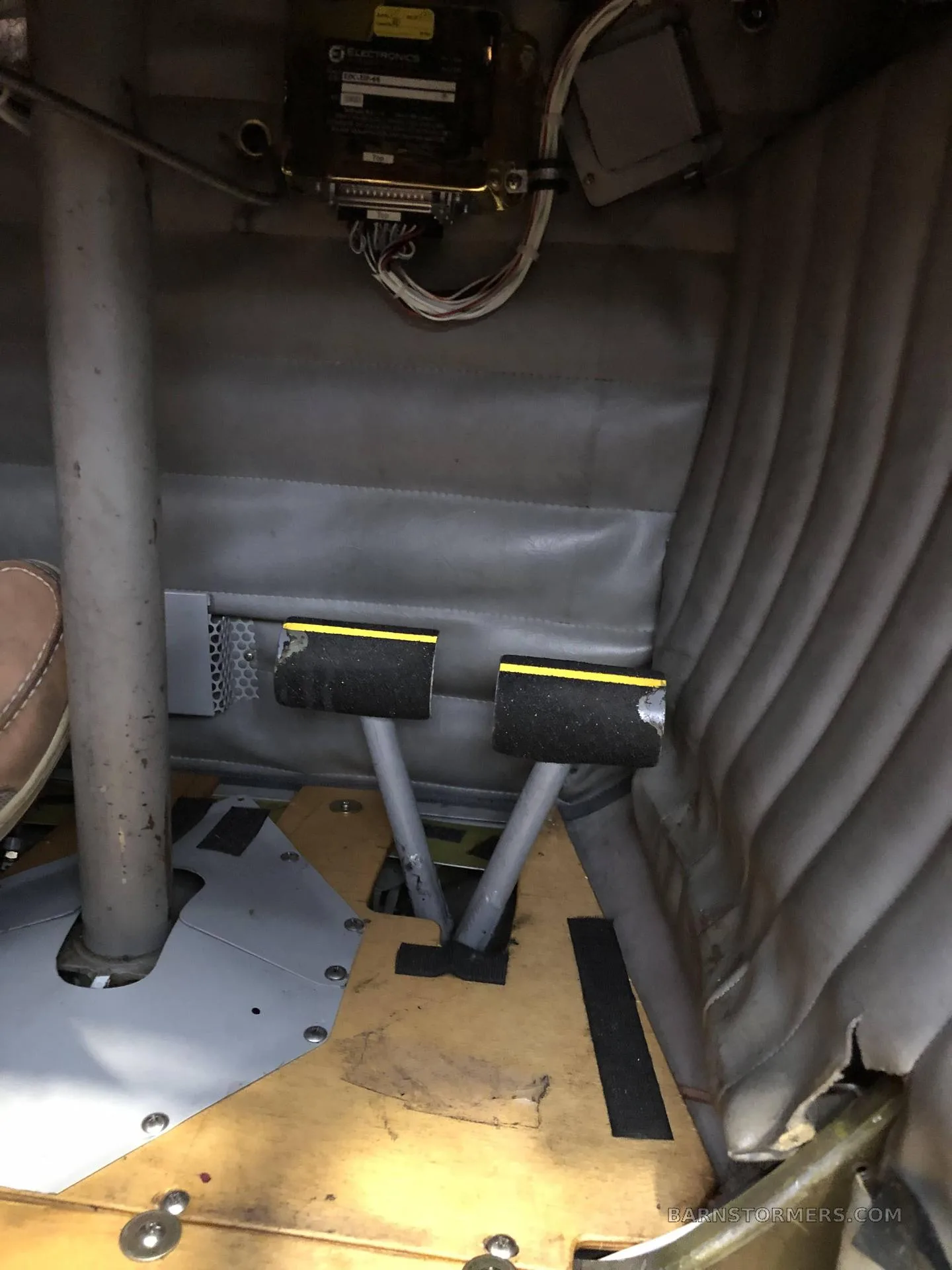 A view of the aircraft's rudder pedals and floor area, showing the grey upholstered side panel.