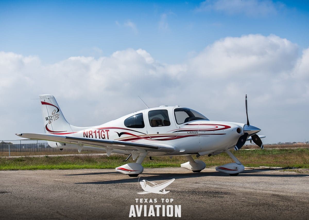 A Cirrus SR22/25 aircraft is parked on the tarmac with a white and red paint scheme.