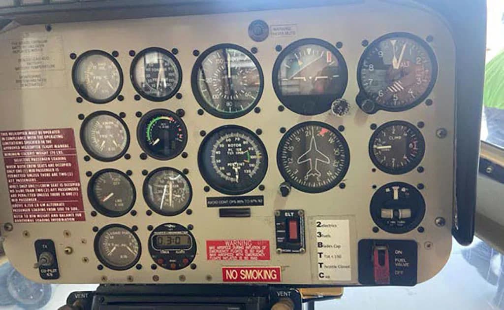A close-up view of a helicopter's instrument panel with various gauges and warning labels.