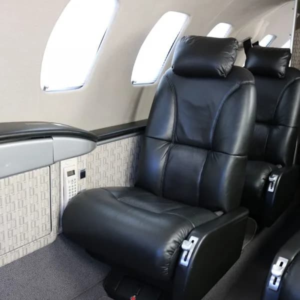 A close-up view of a black leather seat in a private jet cabin next to a window.
