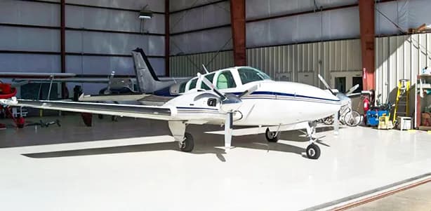 A white and blue Beechcraft Baron sits in a hangar.