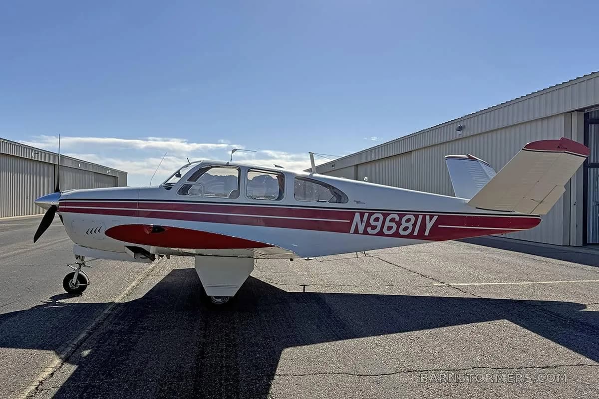 A white single-engine aircraft with red stripes and registration N968IY parked on a tarmac.