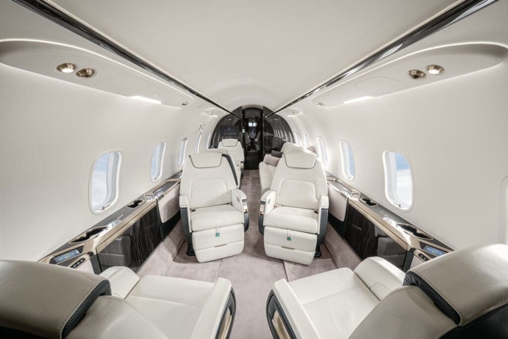 View of the aircraft cabin with white leather seats and dark wood accents.