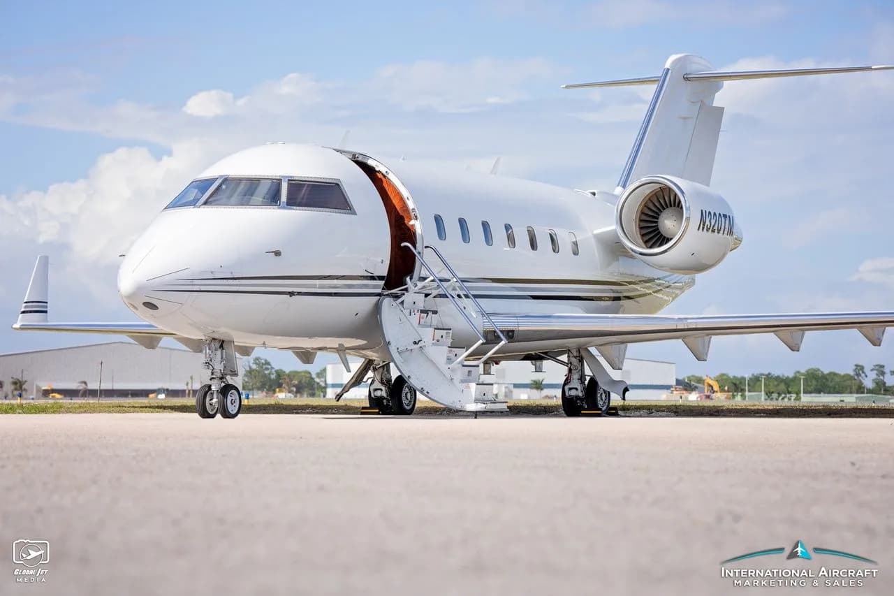 A white jet aircraft with tail number N320TM is parked on the tarmac with the door open and stairs extended.