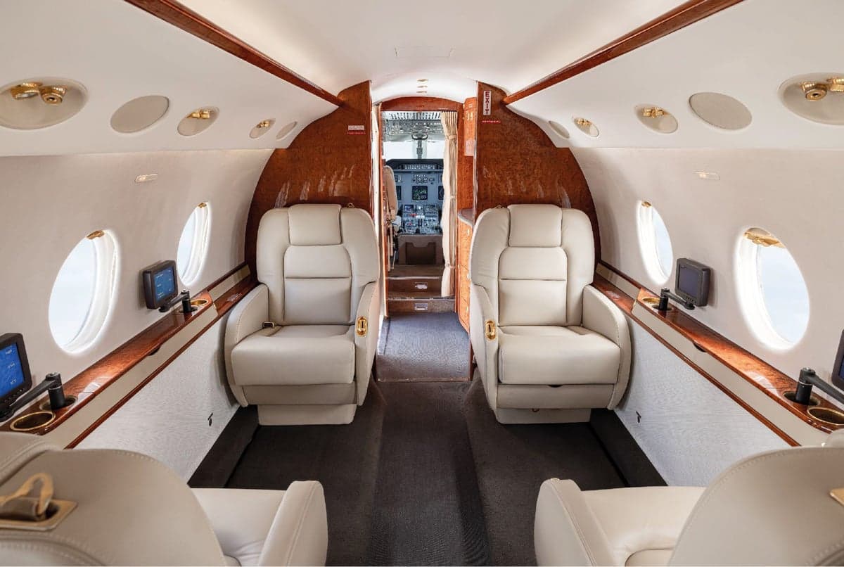Forward cabin of the aircraft featuring leather seats and wood trim.