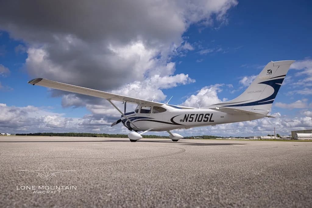 A low-angle side view of the white and blue Cessna 182 Skylane aircraft, N510SL, on an airfield under a blue sky.