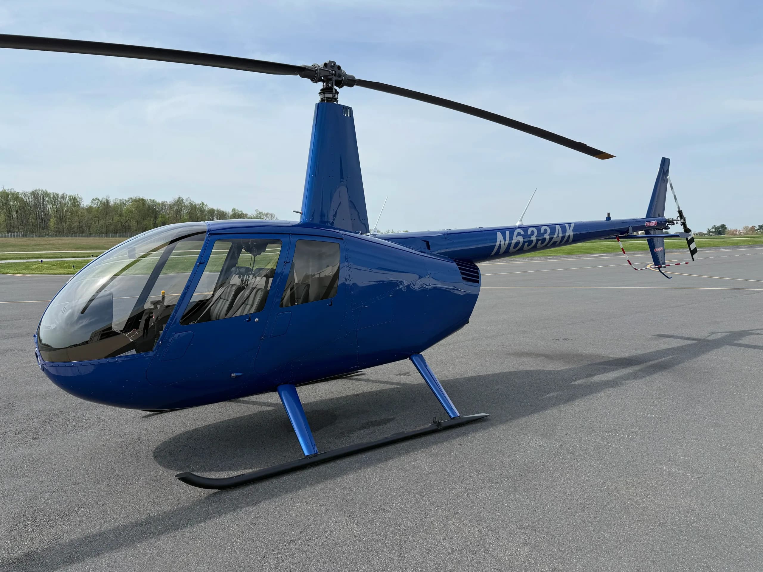 A blue Robinson R44 helicopter, N633AK, parked on an asphalt tarmac with trees in the background.