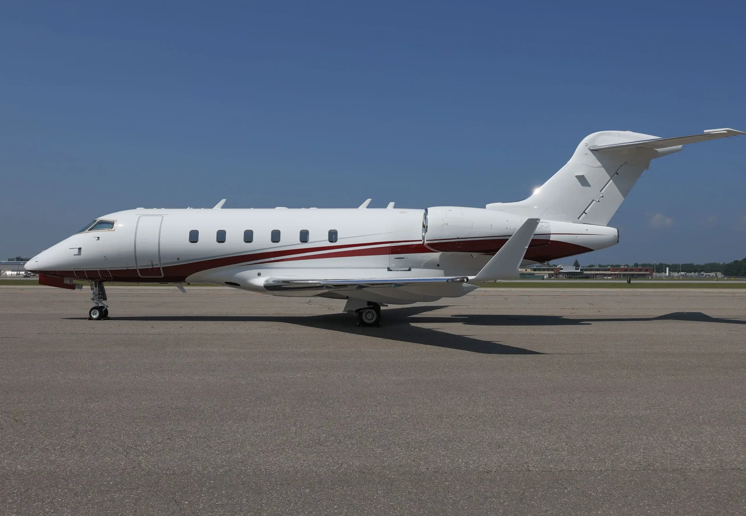 Side view of a white business jet with red and grey stripes, registration N111EL, parked on an airfield.