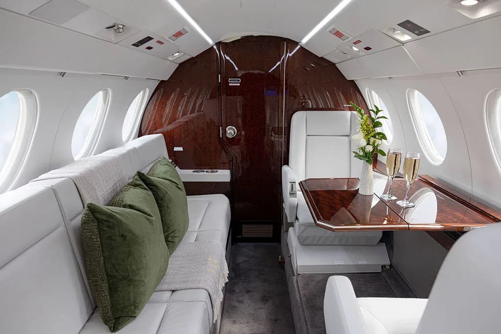 A view of the business jet's cabin showing a light gray couch with green pillows and a table set with champagne flutes.