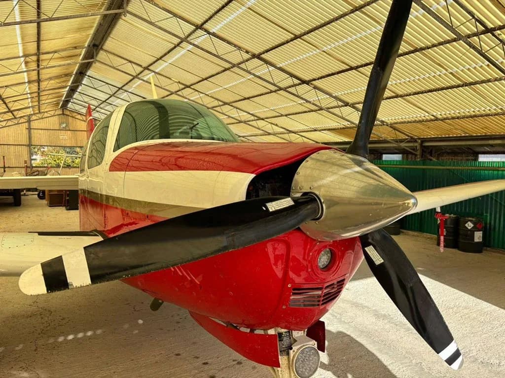 A close-up front view of the red and white aircraft, showing its propeller and nose cone inside a hangar.