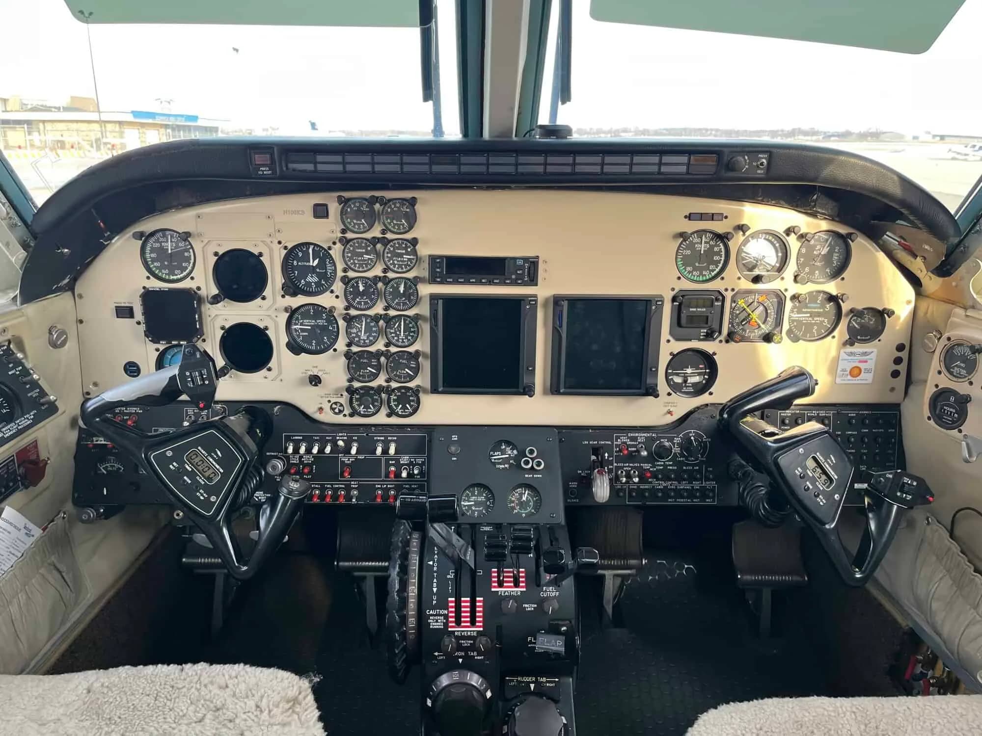 The cockpit of an aircraft, showing a beige instrument panel with analog gauges and two modern display screens.