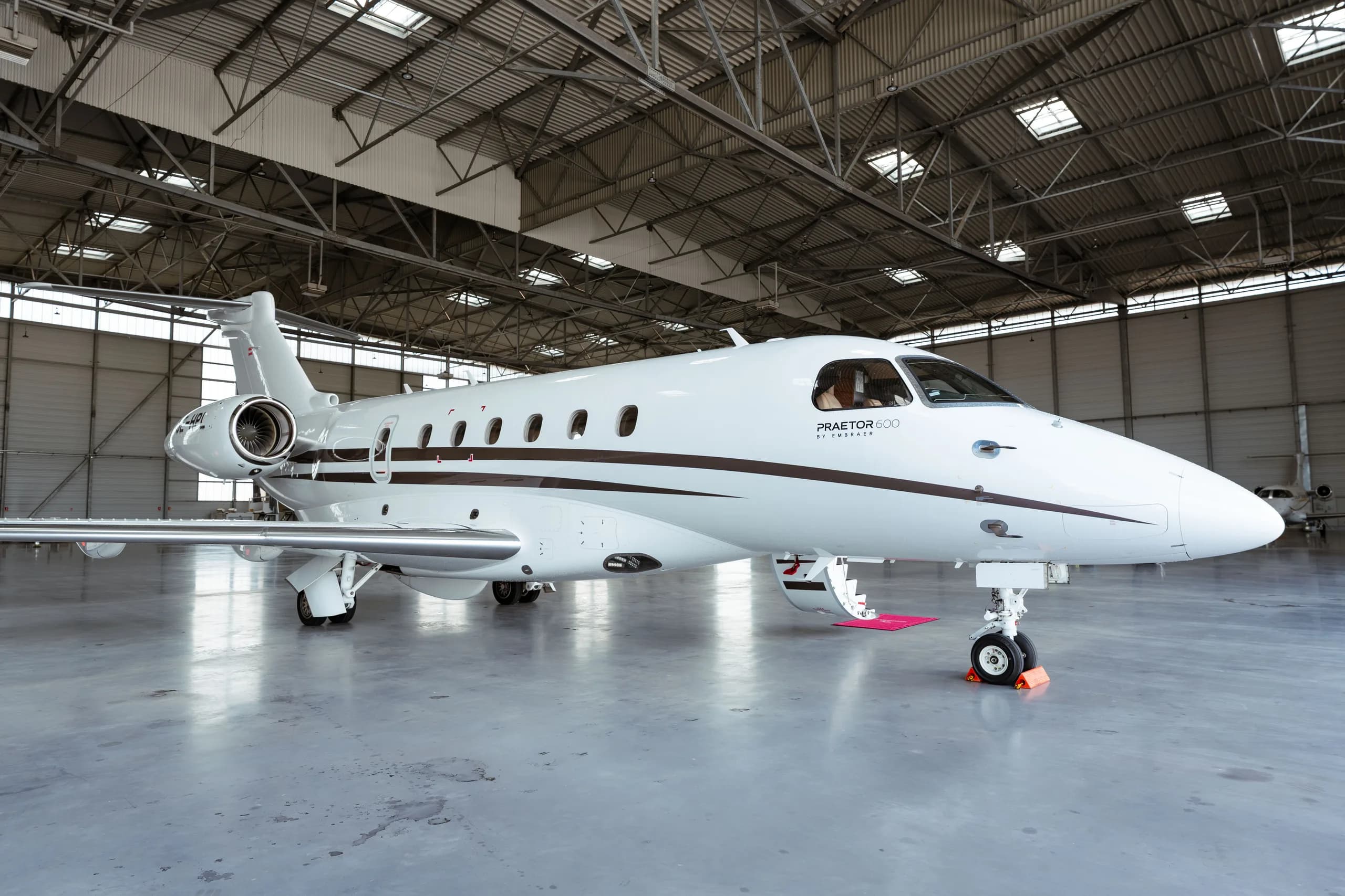 A white Embraer Praetor 600 business jet with brown stripes is parked inside a hangar.