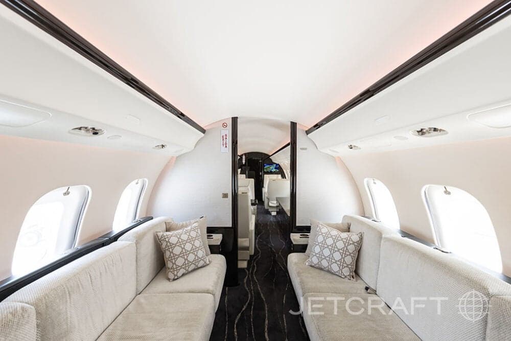 Forward view of the cabin of a Bombardier Global Express with light colored couches and patterned pillows.