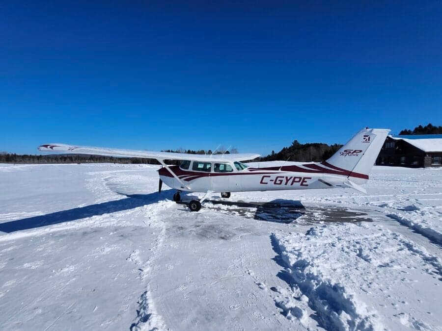 A white and red Cessna 172 (C-GYPE) parked in a vast snowy landscape under a clear blue sky.