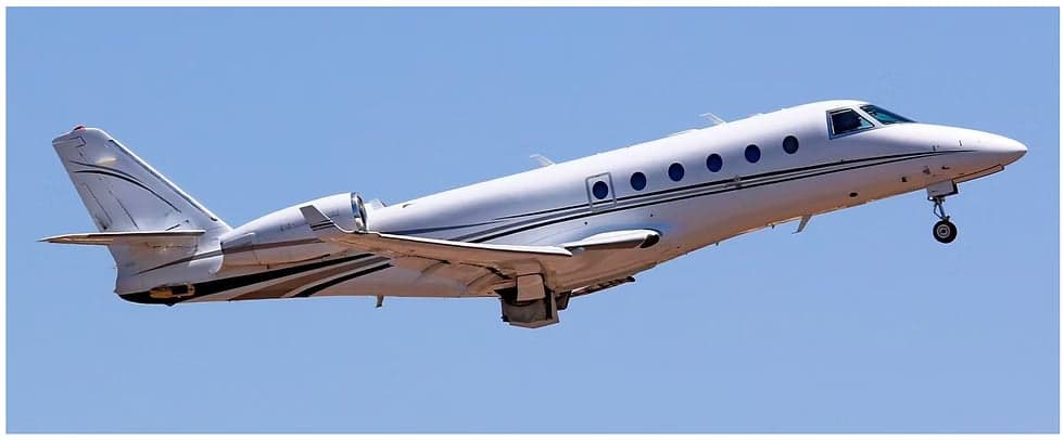 A white jet aircraft with black stripes is taking off against a clear blue sky.