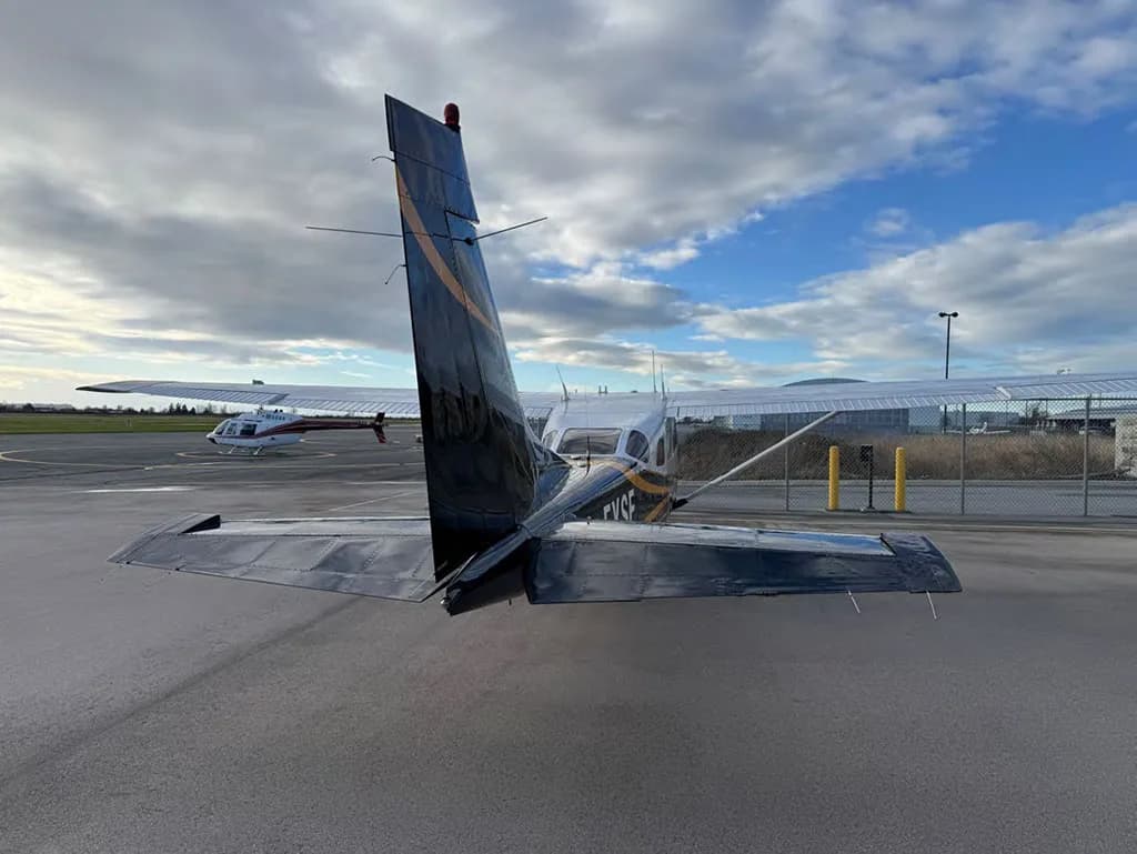 A rear view of the dark green and white Cessna 182, registration C-FYSE, parked on an airfield with another aircraft in the distance.