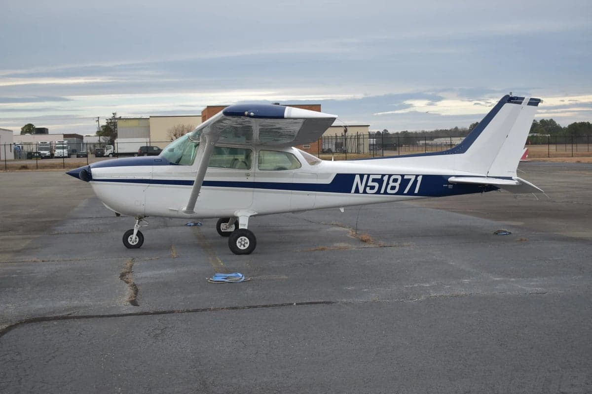 A white Cessna 172 with blue and grey stripes (N51871) is parked on a tarmac, viewed from the right side.
