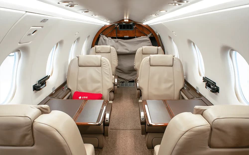 Interior view of a private aircraft cabin with beige leather seats and fold-out tables, looking towards the rear.