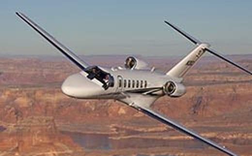 A silver jet aircraft in flight over a desert landscape.