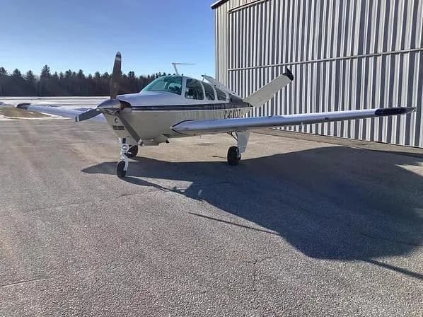 A beige and blue single-engine aircraft with registration C-GXOZ is parked nose-first next to a metal hangar.