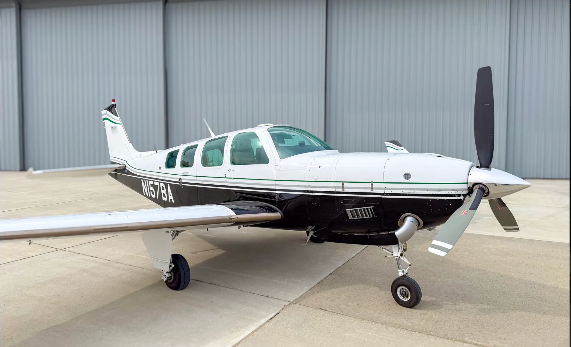 A front-side view of the white and black Beechcraft Baron N157BA with green stripes, parked on an airfield.
