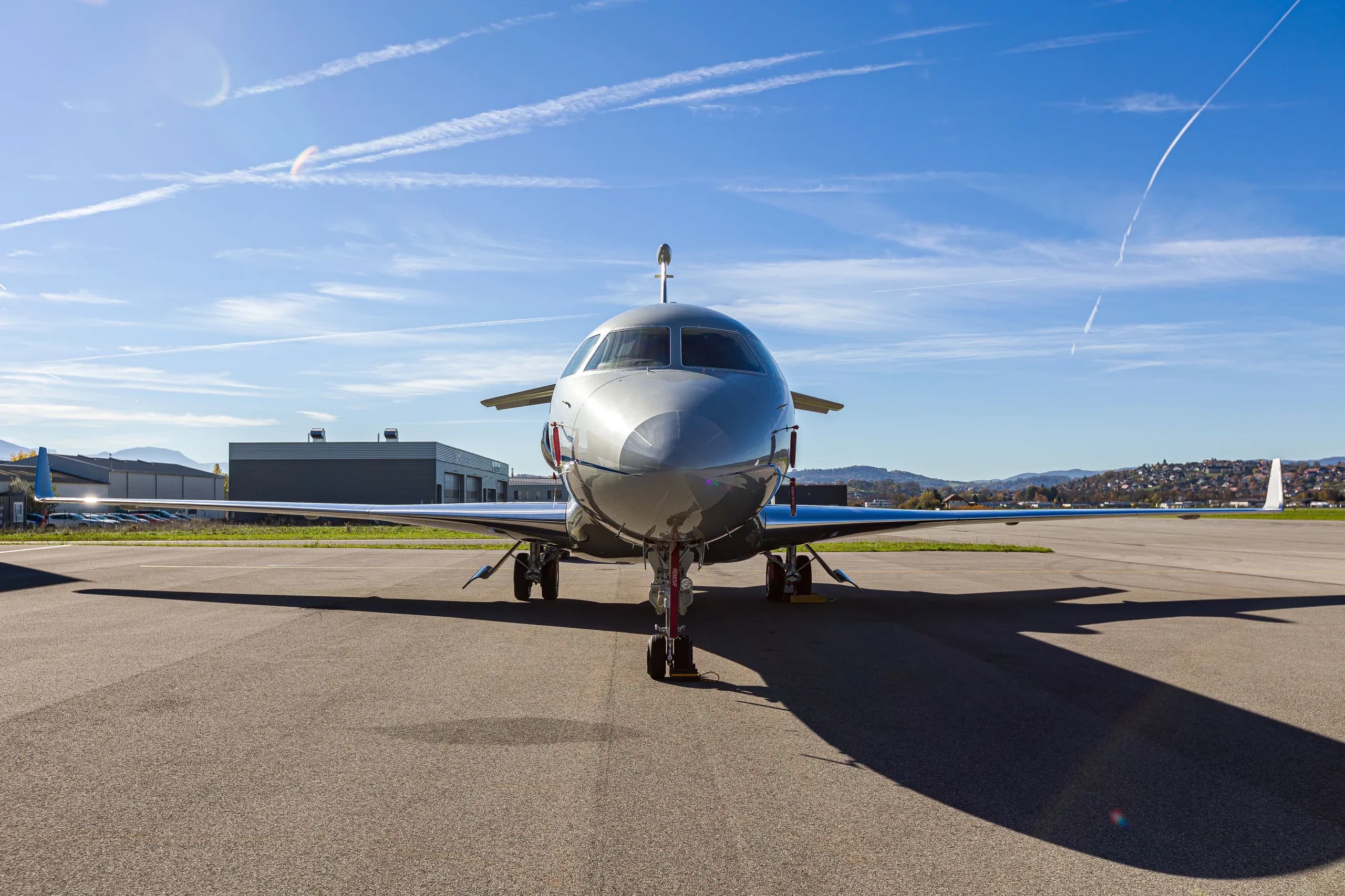 A silver Dassault Falcon 900EX business jet with blue stripes parked head-on on an airfield.