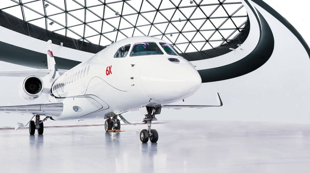 A white Falcon 6X business jet parked in a modern hangar.