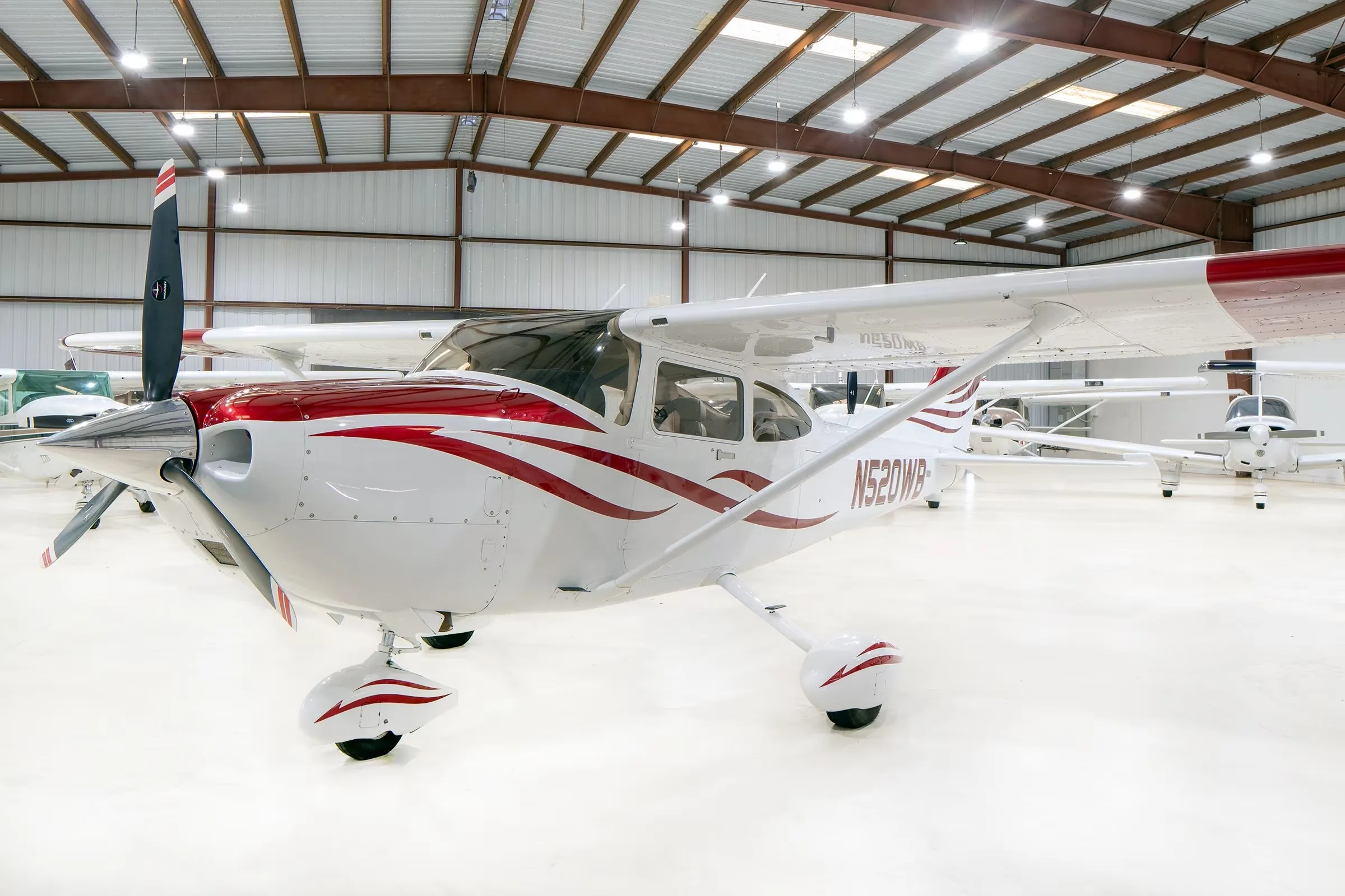 A white Cessna Skylane N520WB with red and grey stripes, parked in a hangar, viewed from the front-left.