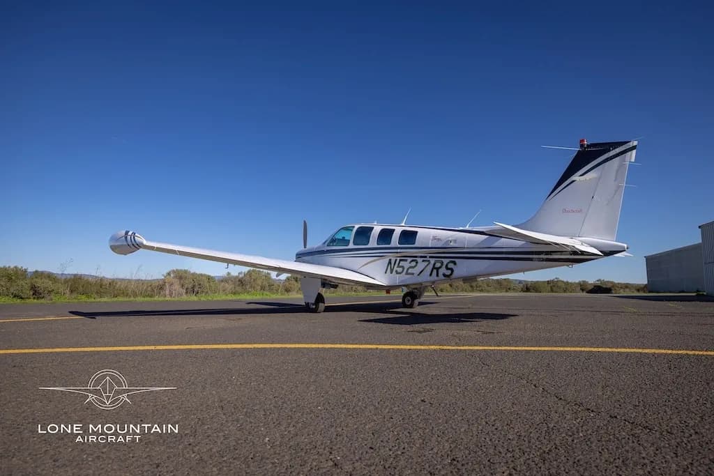 A side view of a white Beechcraft Baron N527RS with black and gold stripes parked on an asphalt runway.