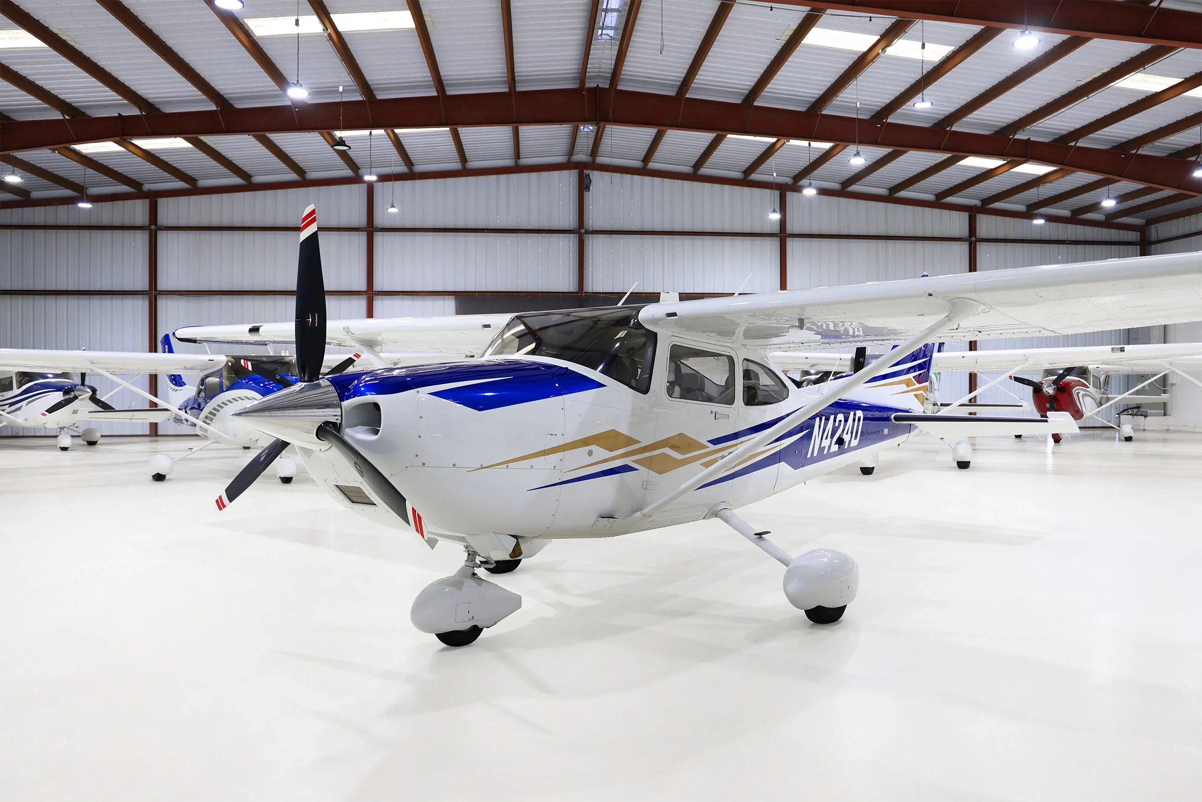 A white and blue Cessna Skylane N424D with gold accents, parked in a hangar.