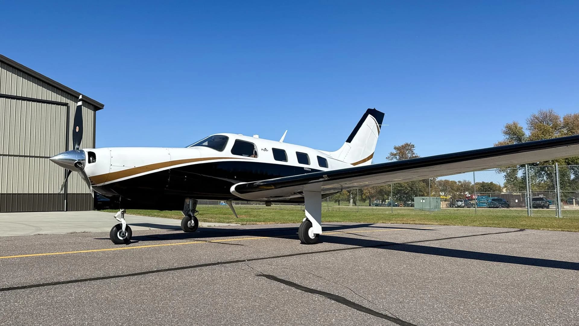 A close-up front-side view of a white and black Piper Mirage N200JP with gold accents on an airfield.