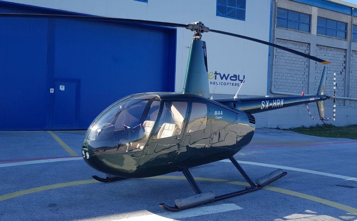 A Robinson R44 Clipper helicopter, registration SX-HRK, parked on a helipad.