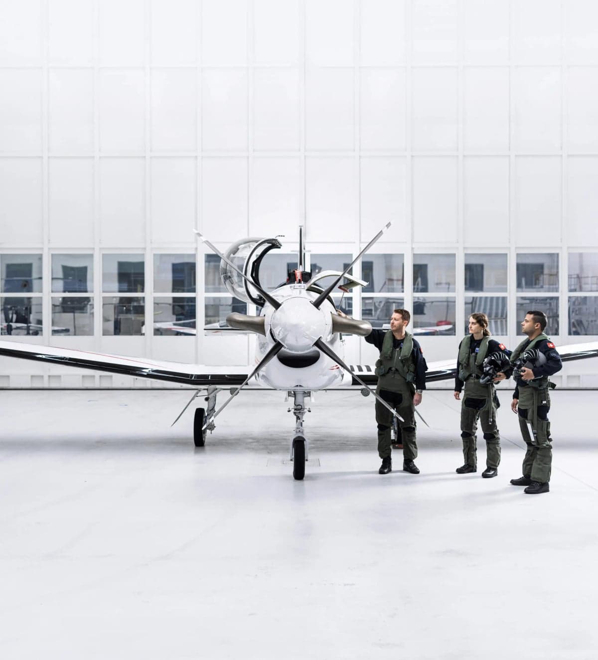 A Pilatus PC-7 MKX aircraft in a hangar with three people in flight suits.