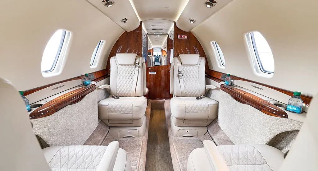 The luxurious interior of a private jet cabin features light-colored quilted leather seats and polished wood accents.