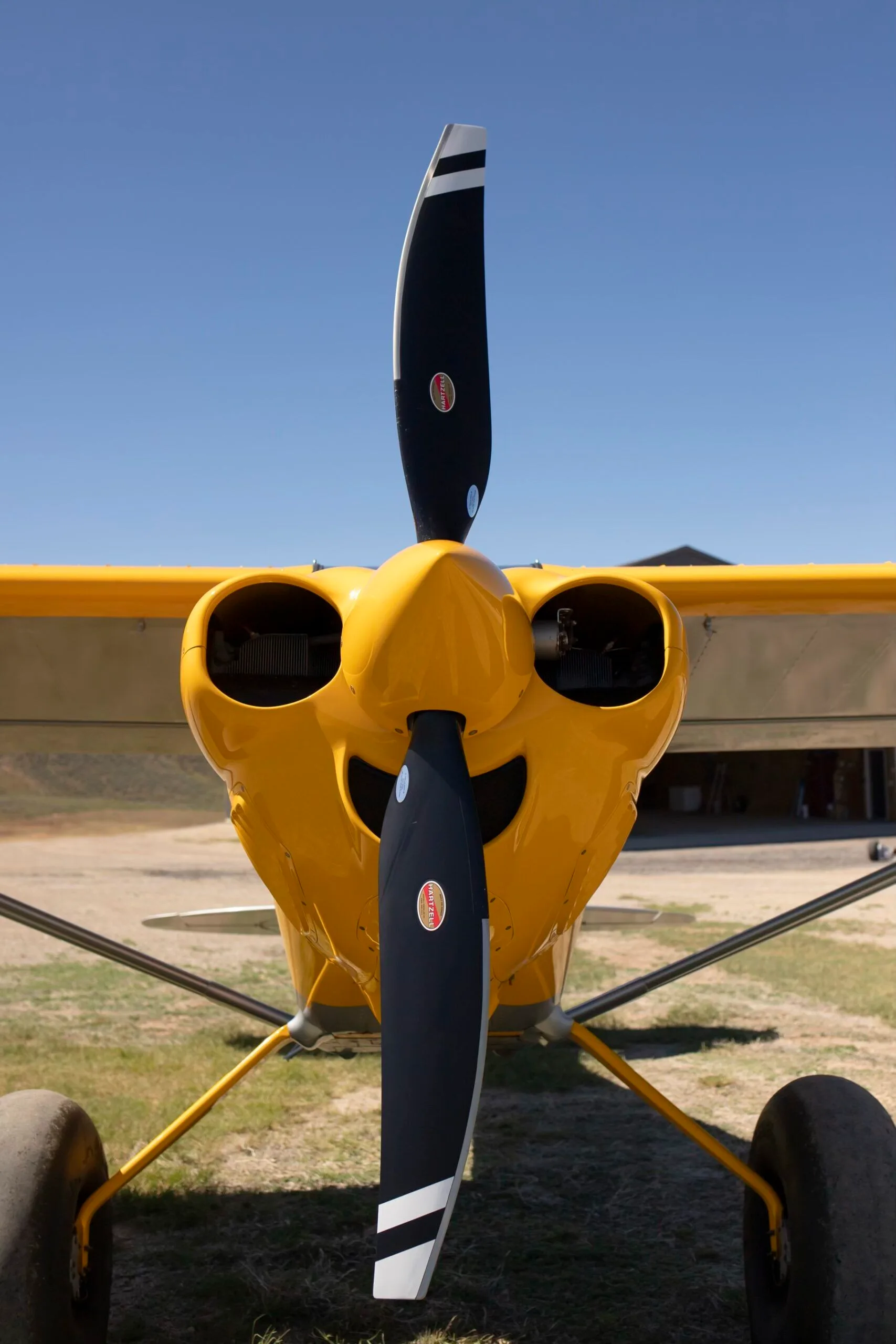A close-up front view of the propeller and engine cowling of a yellow CubCrafters XCub aircraft.