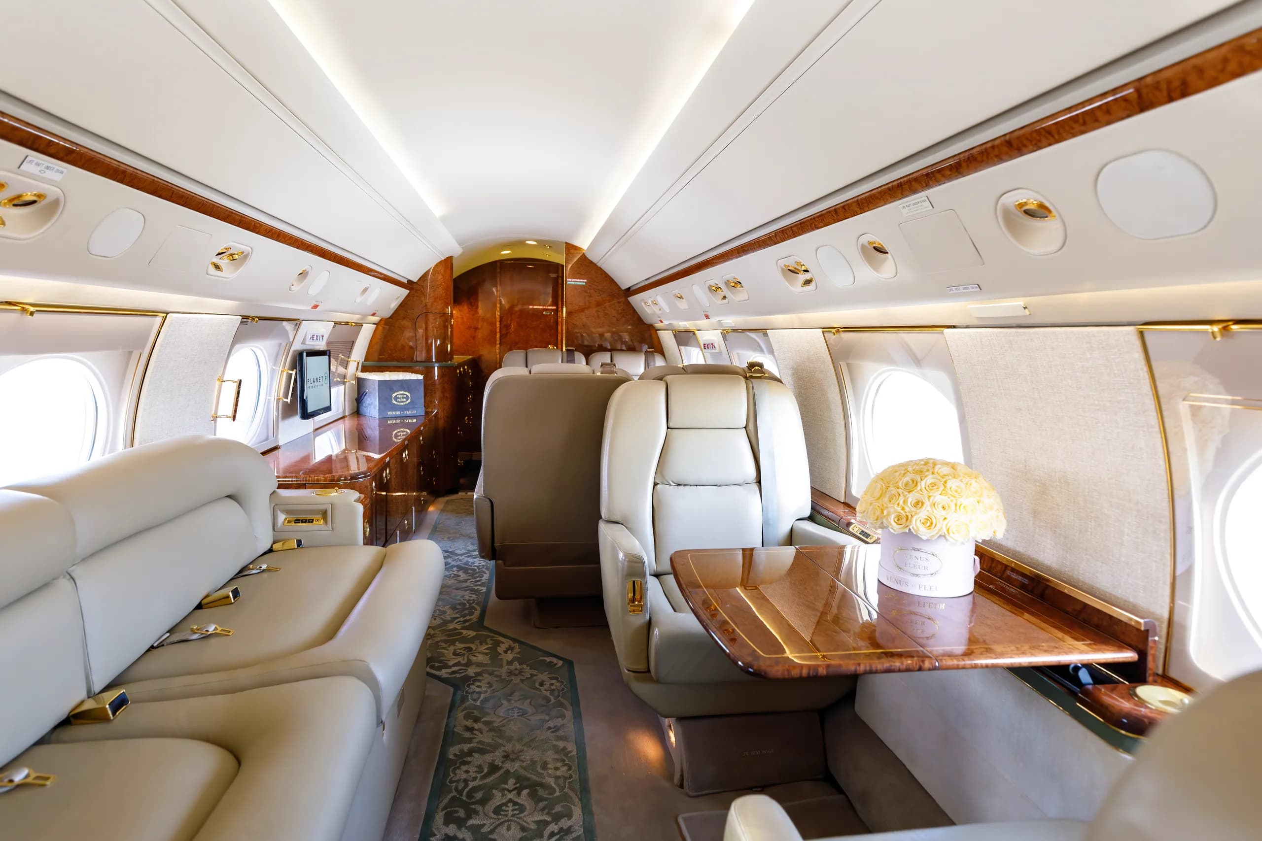 A luxurious aircraft cabin interior with a cream-colored lounge seat, individual seats, and a table adorned with a bouquet of white roses.