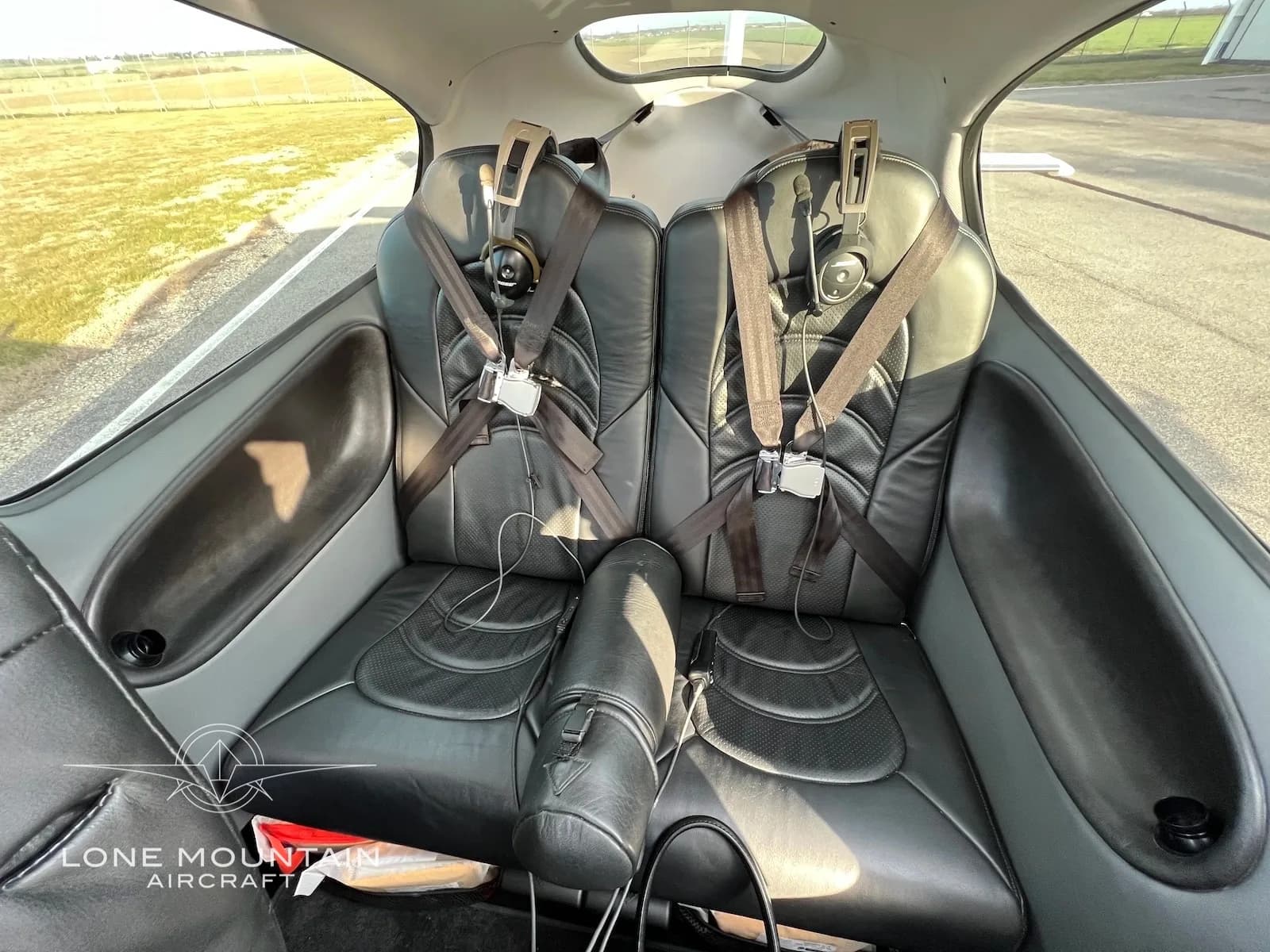 The rear black leather seats of a Cirrus SR22 aircraft cabin, with seatbelts fastened.