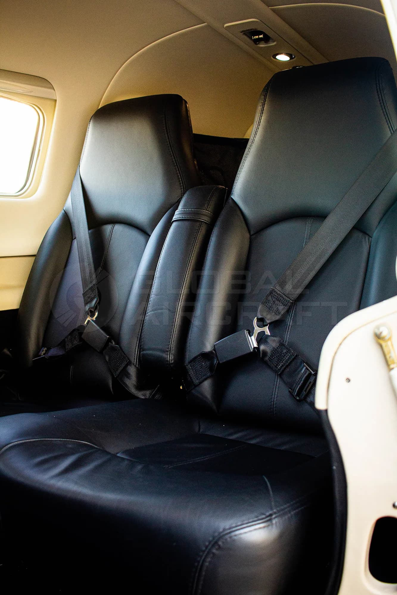 Close-up view of two black leather passenger seats with seatbelts in an aircraft cabin.