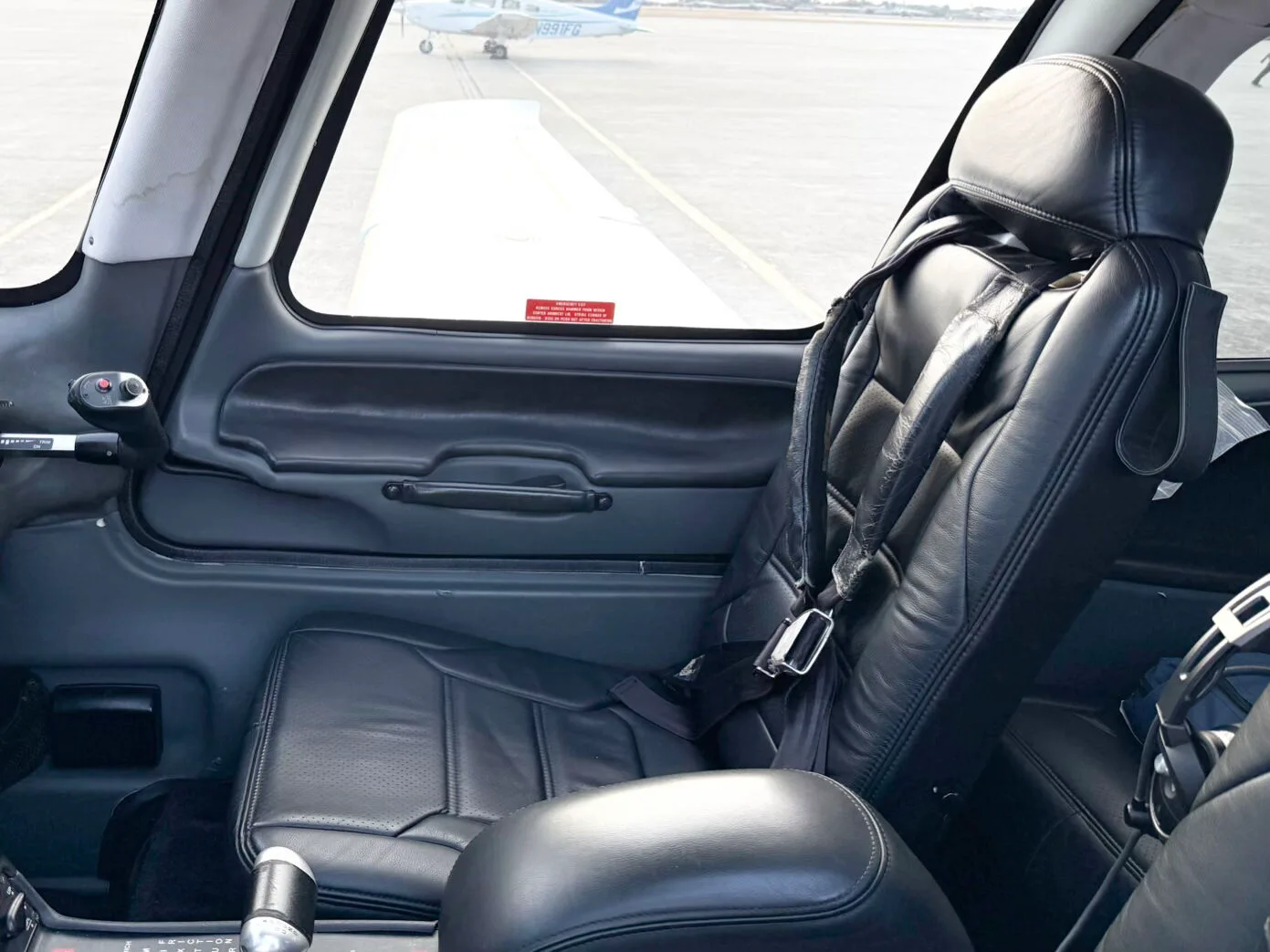 The black leather pilot's seat and side panel of a Cirrus SR22 aircraft, looking out onto the tarmac.