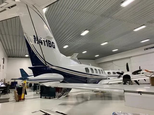 A white and blue twin-engine turboprop aircraft, N411BG, is parked in a hangar, viewed from the rear-right.