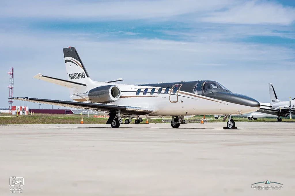 A white and dark grey Cessna Citation V (N550RB) business jet is parked on a tarmac under a blue sky.