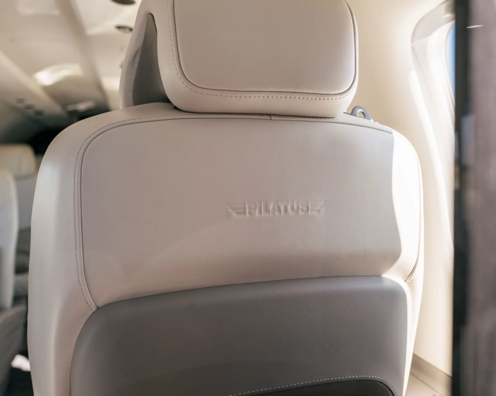 A close-up of an aircraft seat with the "PILATUS" logo embossed on the light-colored leather headrest.