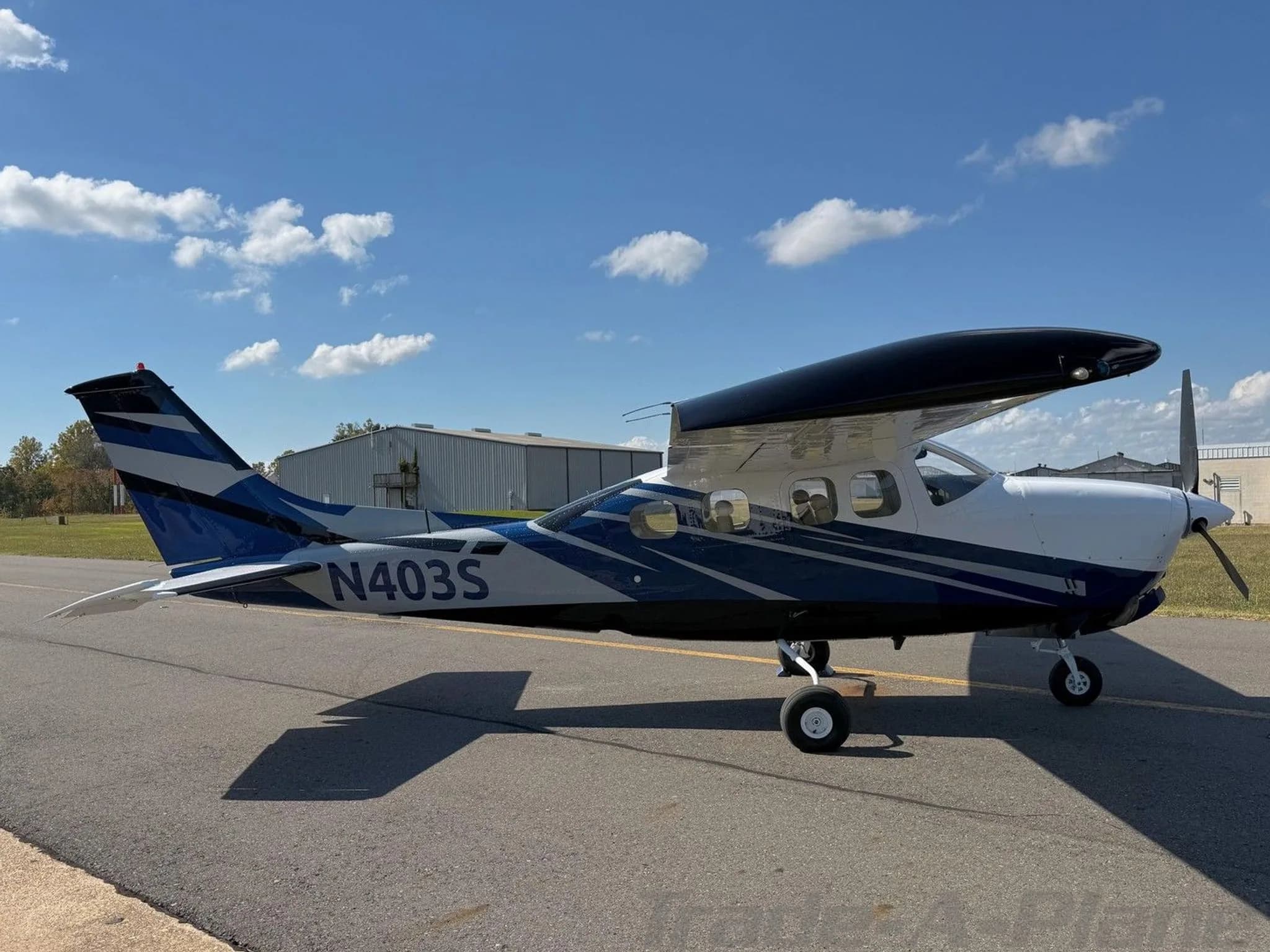 A side view of a white and blue Cessna 210 Centurion aircraft (N403S) parked on an airfield.