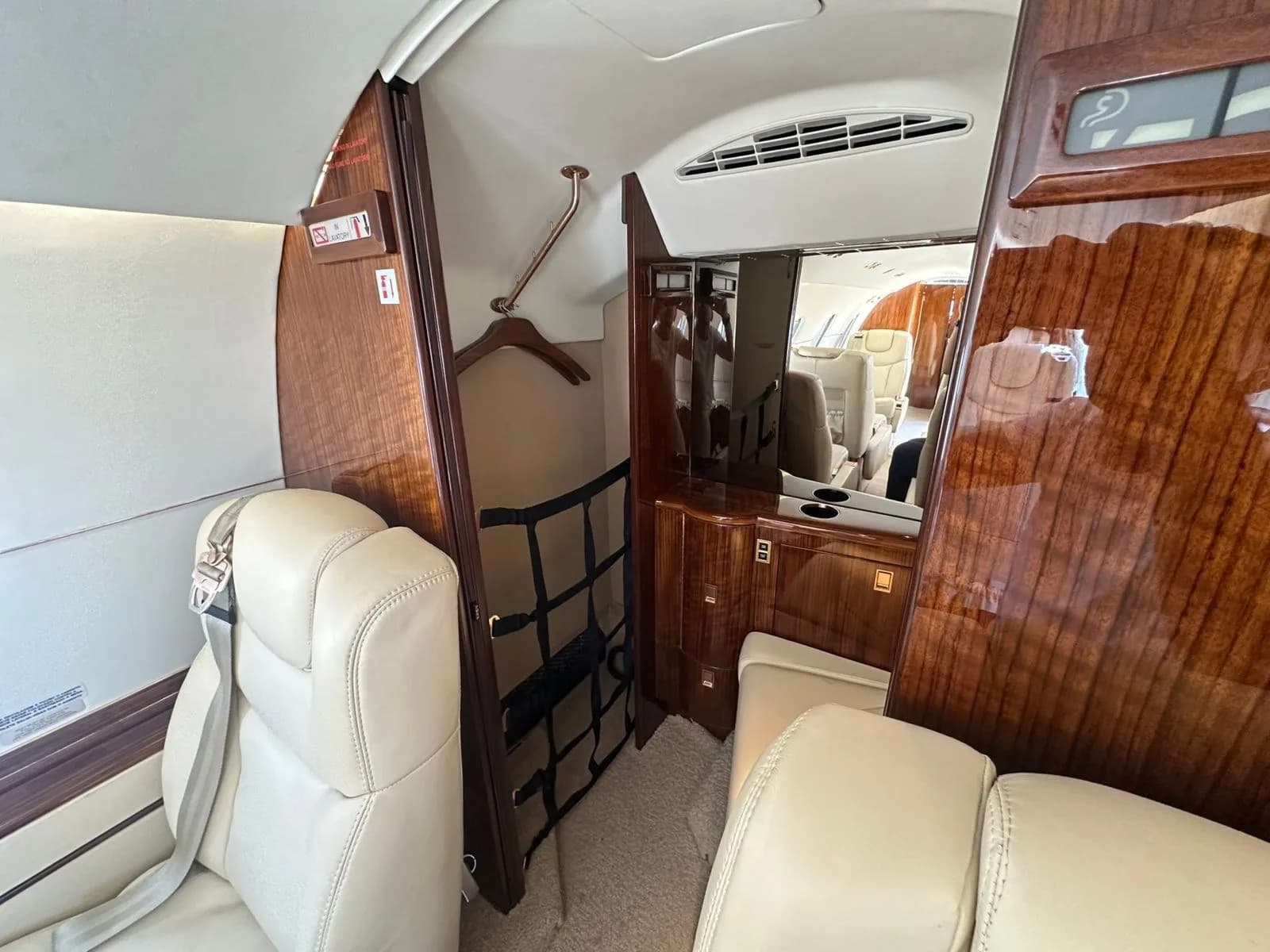 A section of the aircraft's interior showing a wardrobe area with a hanger, storage net, and polished wood paneling.